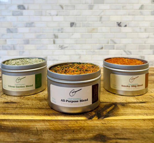 Three metal containers of different spice blends on a wooden surface with a marble backsplash.
